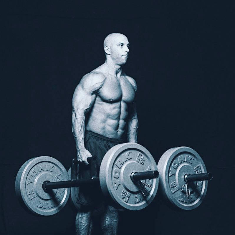 Christian Thibaudeau walking with two weighted bars, showing his large chest, abs and shoulders