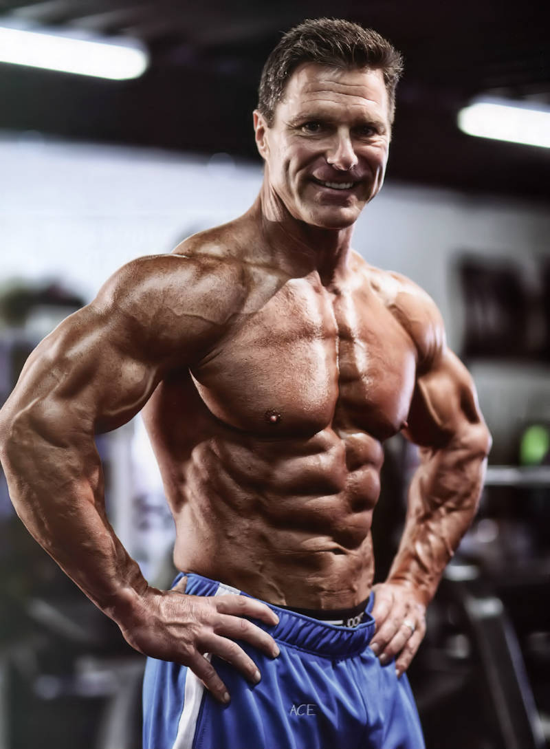 Clark Bartram looking incredibly lean and muscular standing with his shirt off in the gym