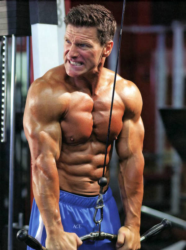 Clark Bartram completing a tricep pulldown, showing off his large triceps, chest and ripped abs