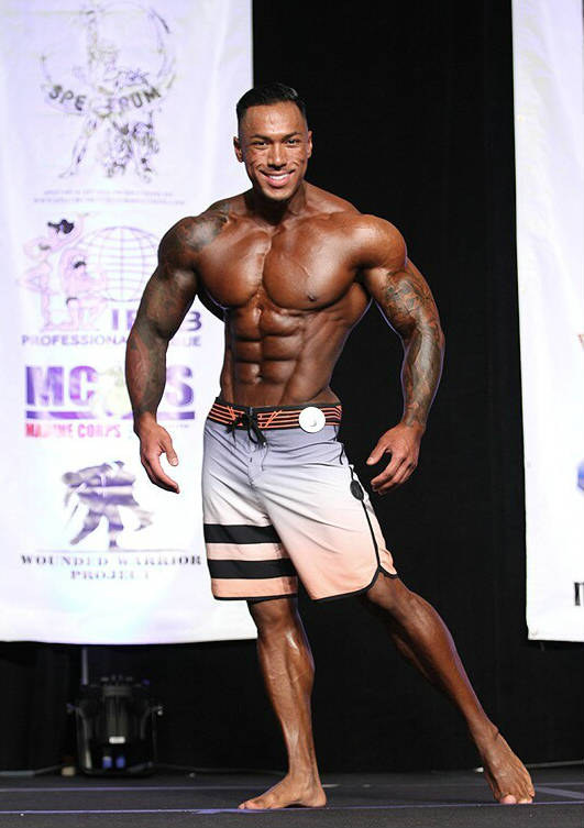 Dean Balabis posing at a physique competition, showing off his ripped abs, tapered waist and large delts