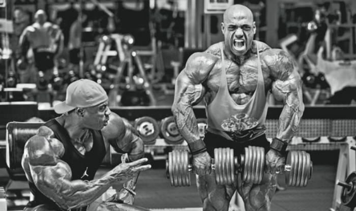 Dennis James completing a dumbbell shoulder lift, showing his large delts, arms and quads