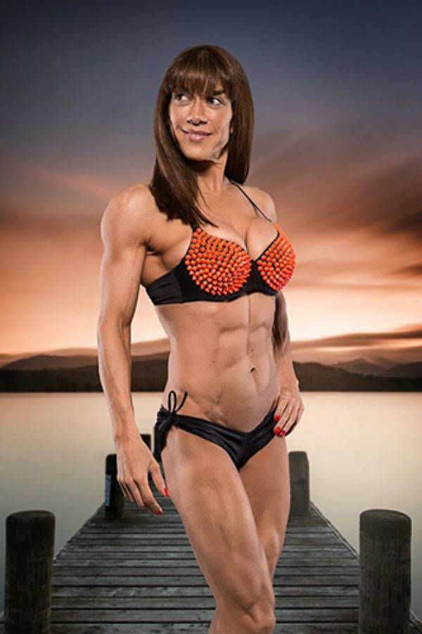 Donna De Lisser standing in front of a green screen. displaying her abs and big deltoids