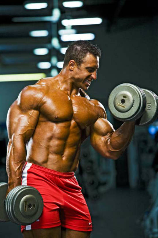 Erik Fankhouser completing a dumbbell curl and gritting his teeth while his bicep is worked hard