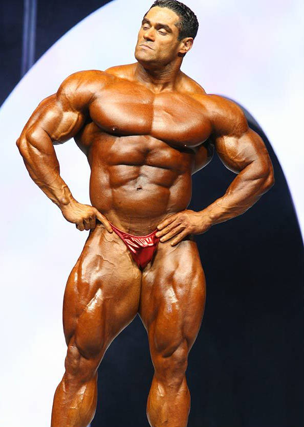 Gustavo Badell posing ta acompetition in a confident stance, showing his large abs, chest and huge quads