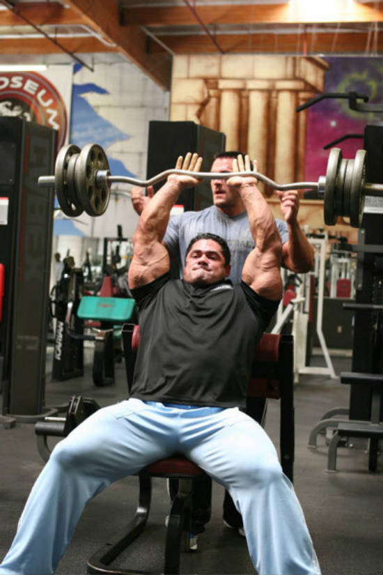 Gustavo Badell completing a barbell tricep exercise in the gym with a spotter 