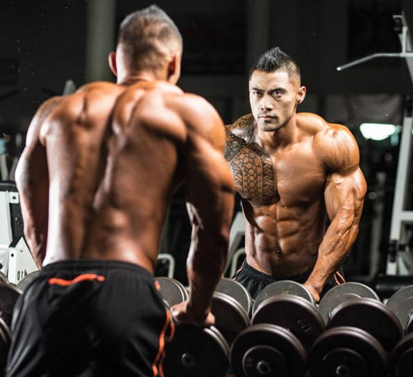 Jake Alvarez holding dumbbells and looking into the gym mirror