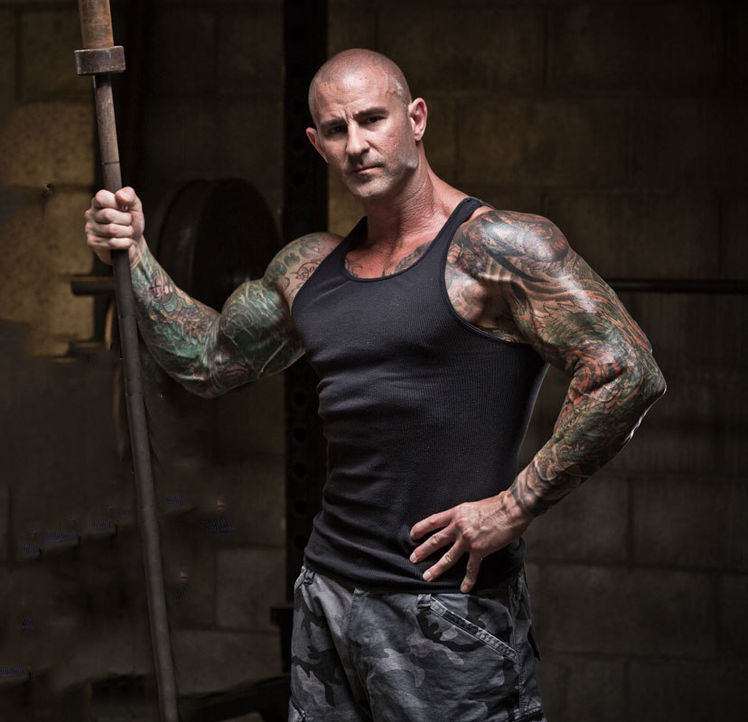 Jim Stoppani posing for the camera holding a barbell looking lean and muscular