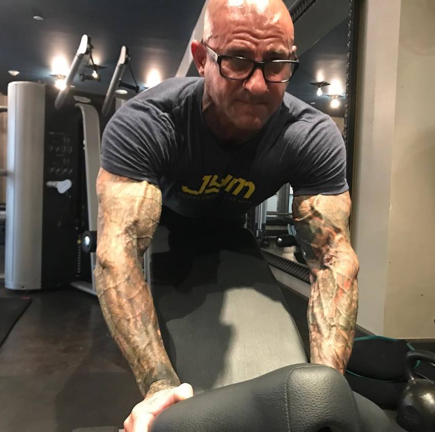 Jim Stoppani doing a push-up variation on an incline bench with his vascular, tattooed, and ripped arms