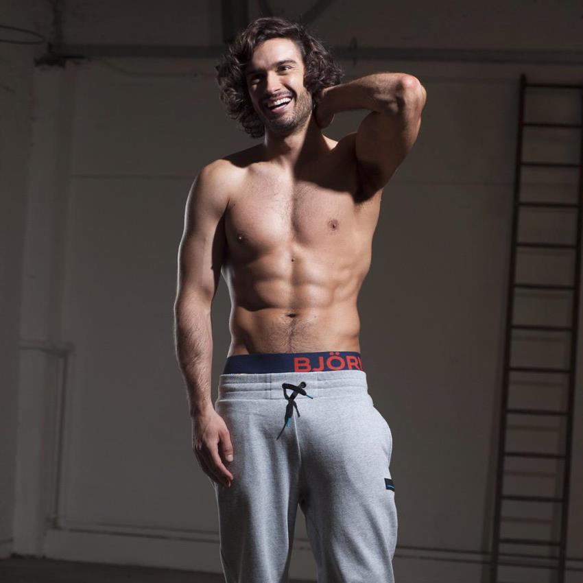 Joe Wicks in grey track pants, smiling and showing his lean upper physique