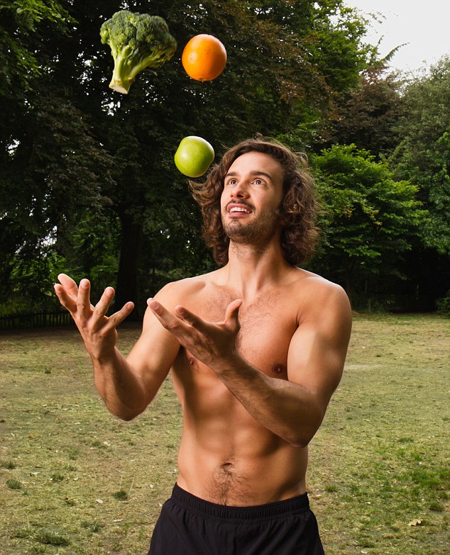 Joe Wicks juggling an orange, apple, and broccoli as he stands in the forest shirtless, displaying his fit upper body