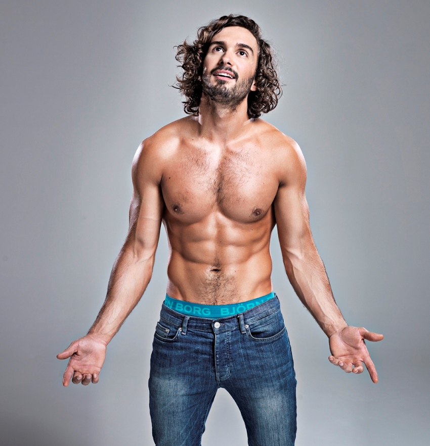 Joe Wicks posing shirtless for a photoshoot, showing his oiled up, fit body