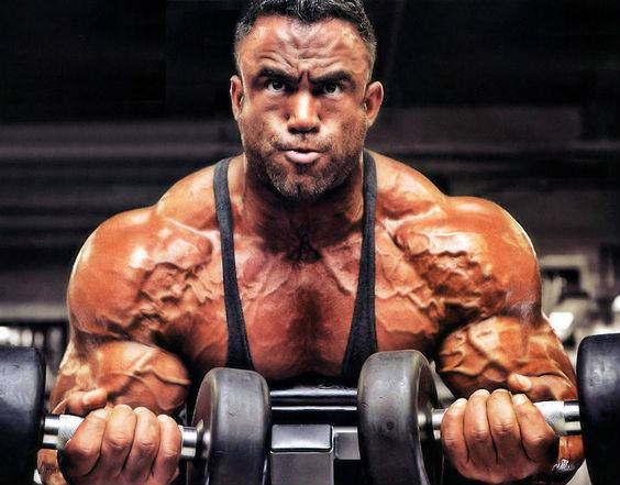 Jose Raymond completing a dumbbell curl with two weights, displaying his well-built shoulders and arms