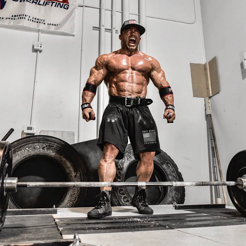 Jose Raymond standing in front of a barbell screaming and showing his well-built upper body