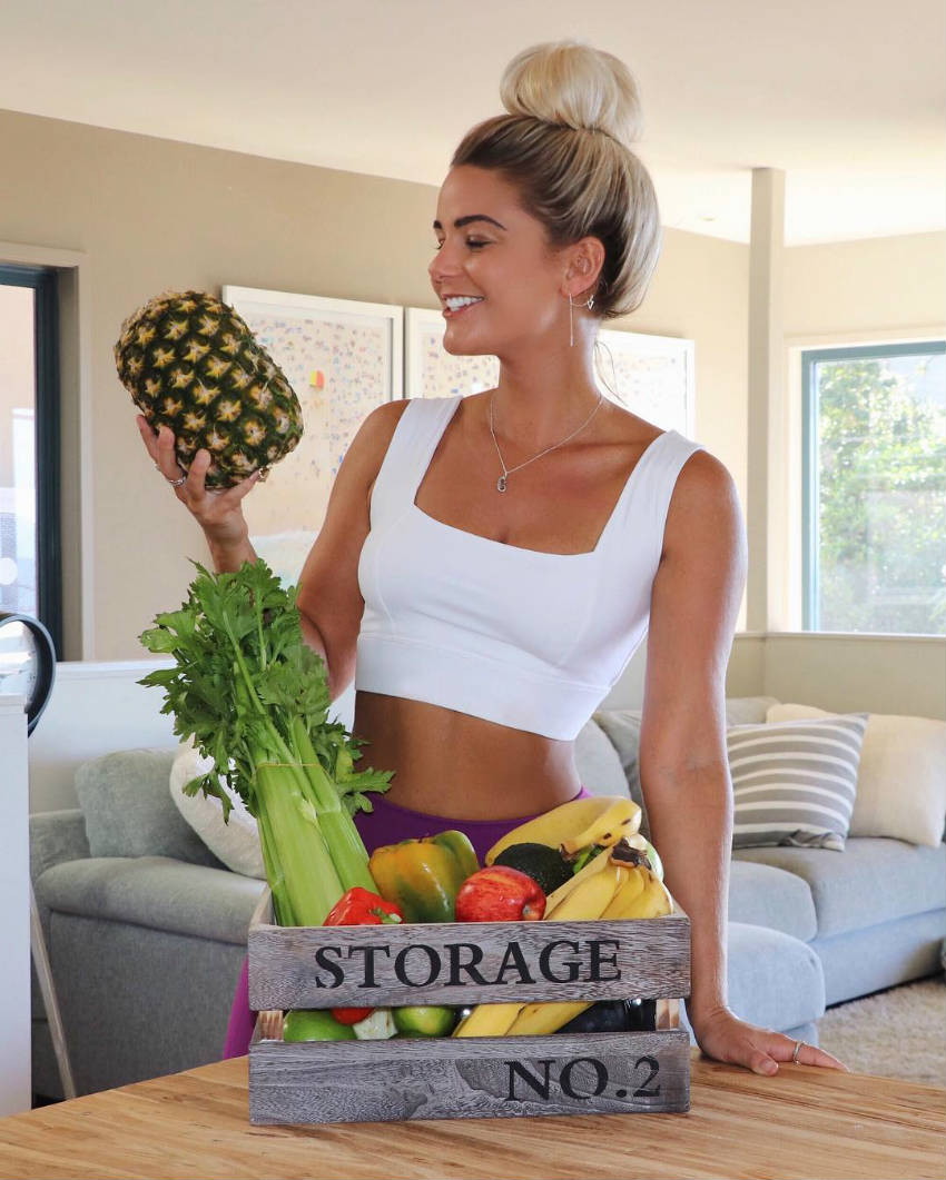 Karina Irby holding a pineapple, showing off her toned arms and abs