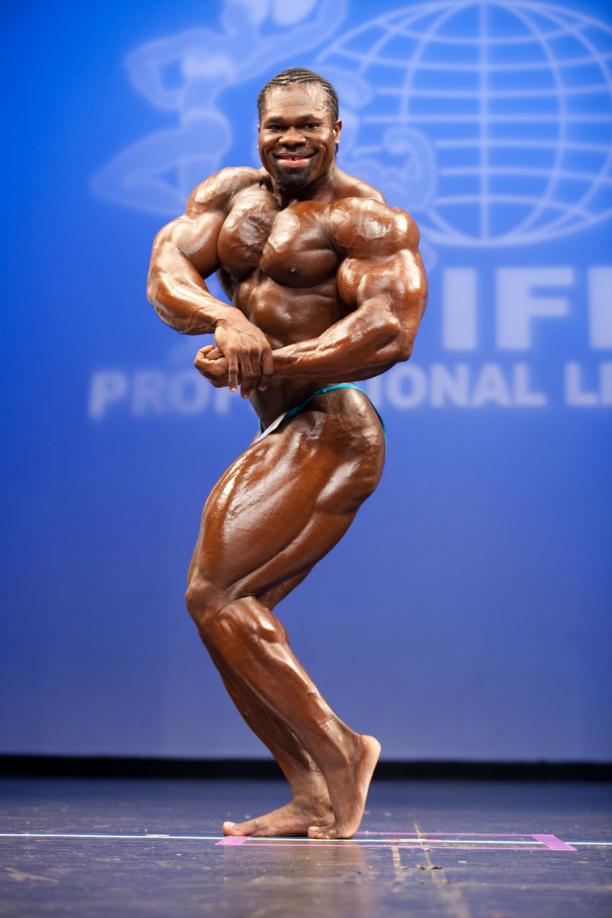 Lionel Beyeke in a side chest pose on a bodybuilding stage