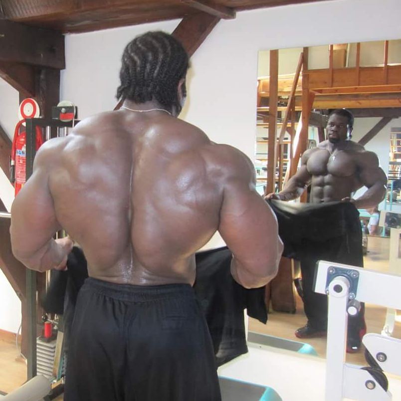 Lionel Beyeke shirtless in front of a mirror, displaying his incredible back width and thickness