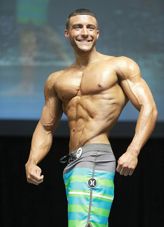 Matt Acton standing in board shorts, showing his ripped abs