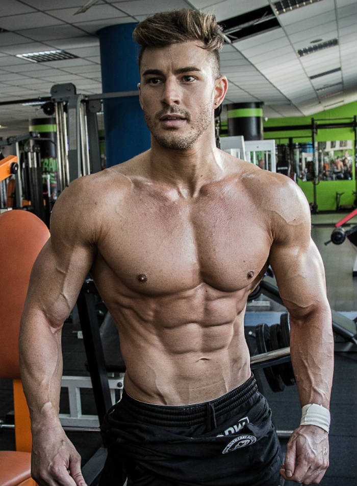 Maxime Parisi looking ripped in the gym, showing his ripepd abs, large arms and toned delts