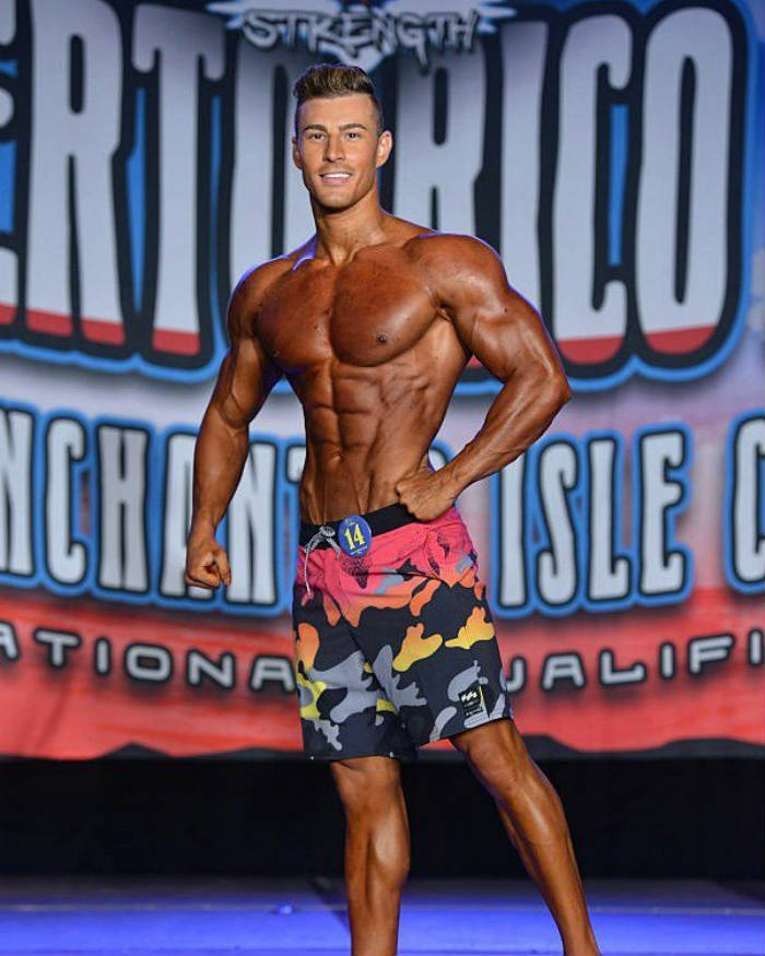 Maxime Parisi posing on a bodybuilding stage looking lean