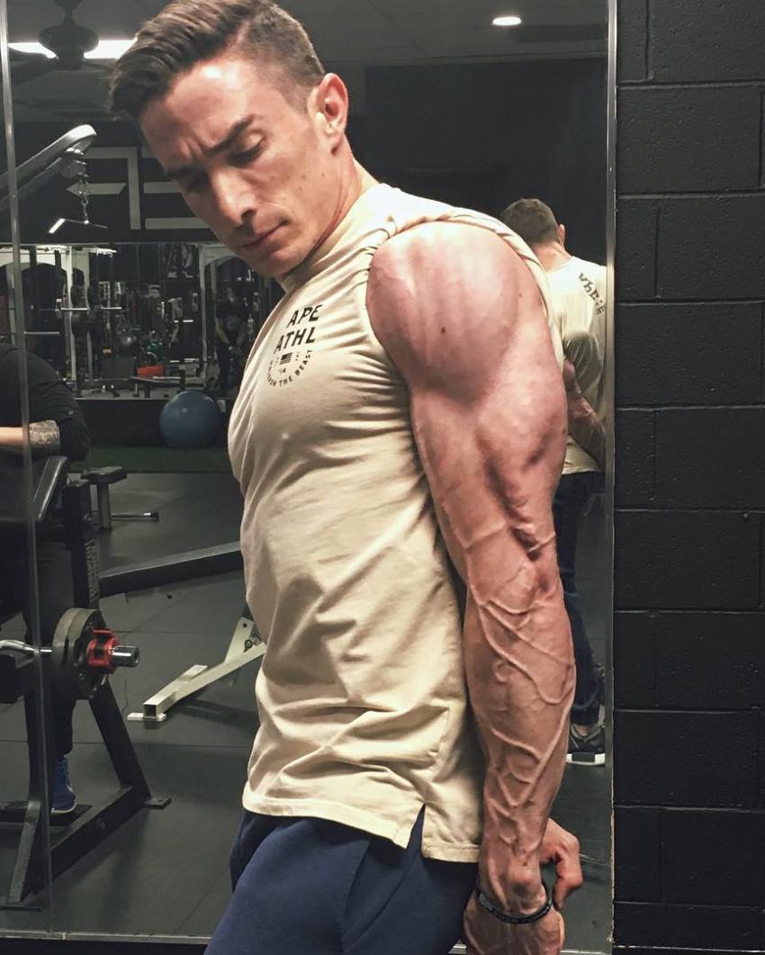 Maxx Chewning doing a side triceps pose in the gym, revealing his strong, lean, and vascular arms