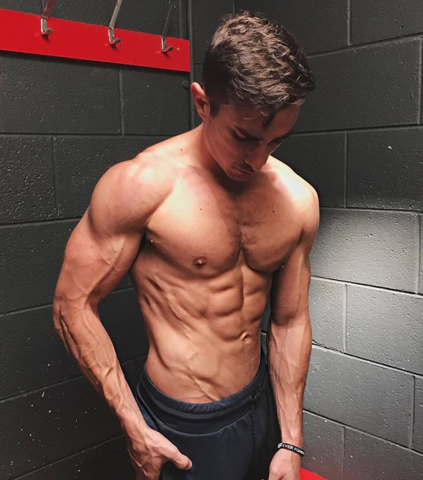 Maxx Chewning shirtless in a dressing room, flexing his abs, chest, and arms