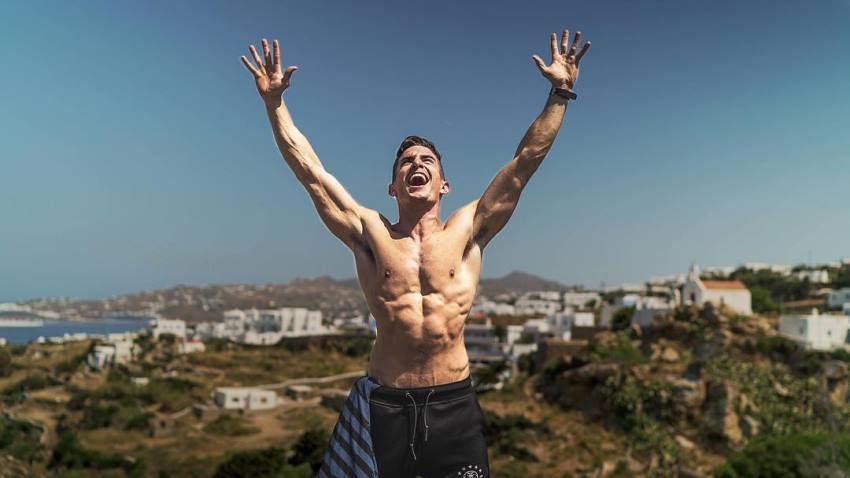 Maxx Chewning standing shirtless outdoors in nature, having his hands in the air while yelling at sky