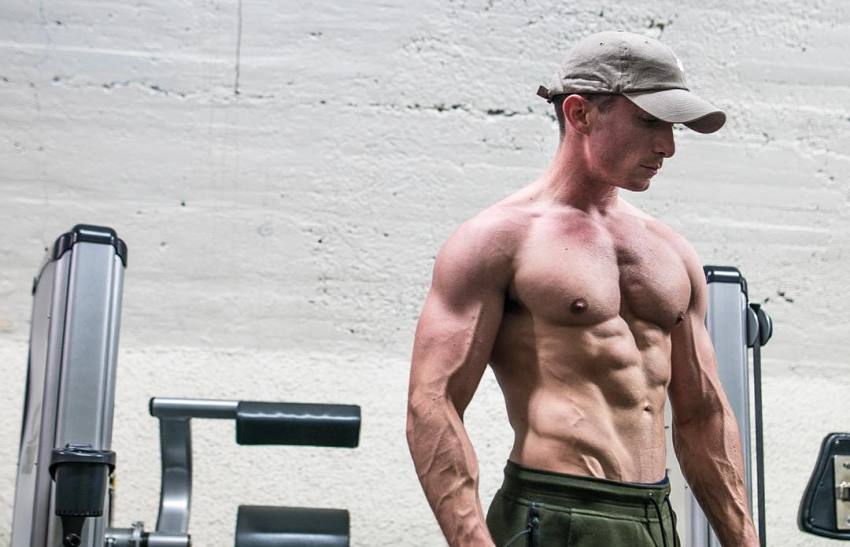 Maxx Chewning standing shirtless, showing his muscular and lean physique as he looks down at the floor