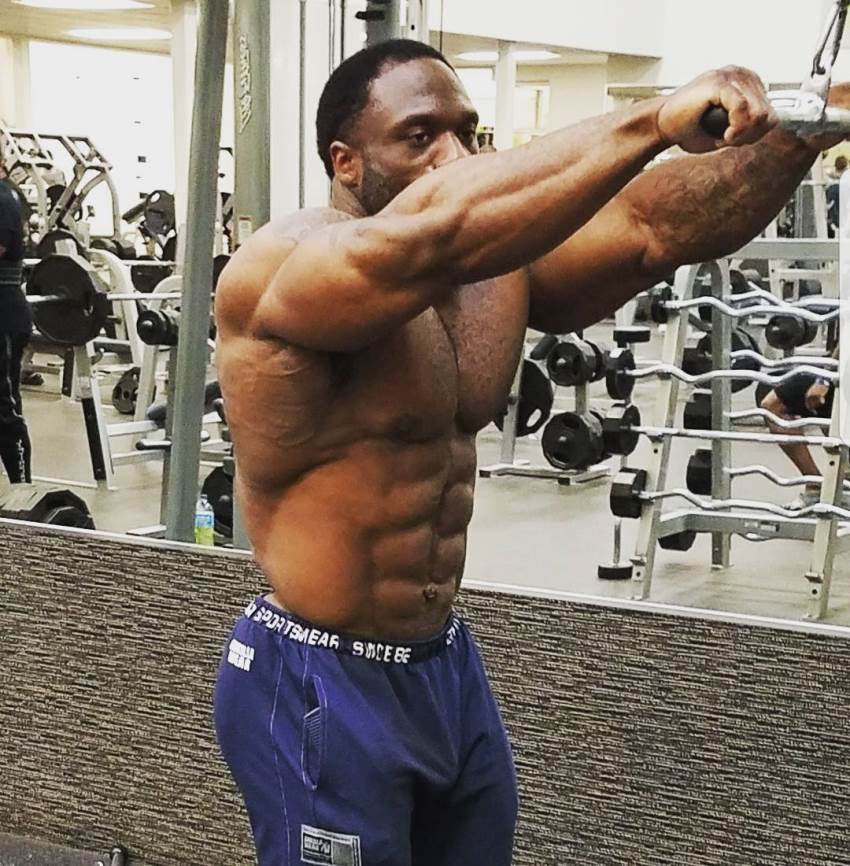 Michael Lockett doing an exercise on a cable machine, being shirtless, looking ripped and muscular