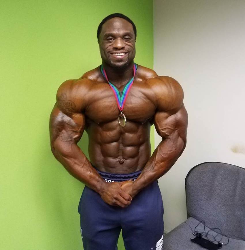 Michael Lockett posing shirtless for the camera, having a gold medal around his neck