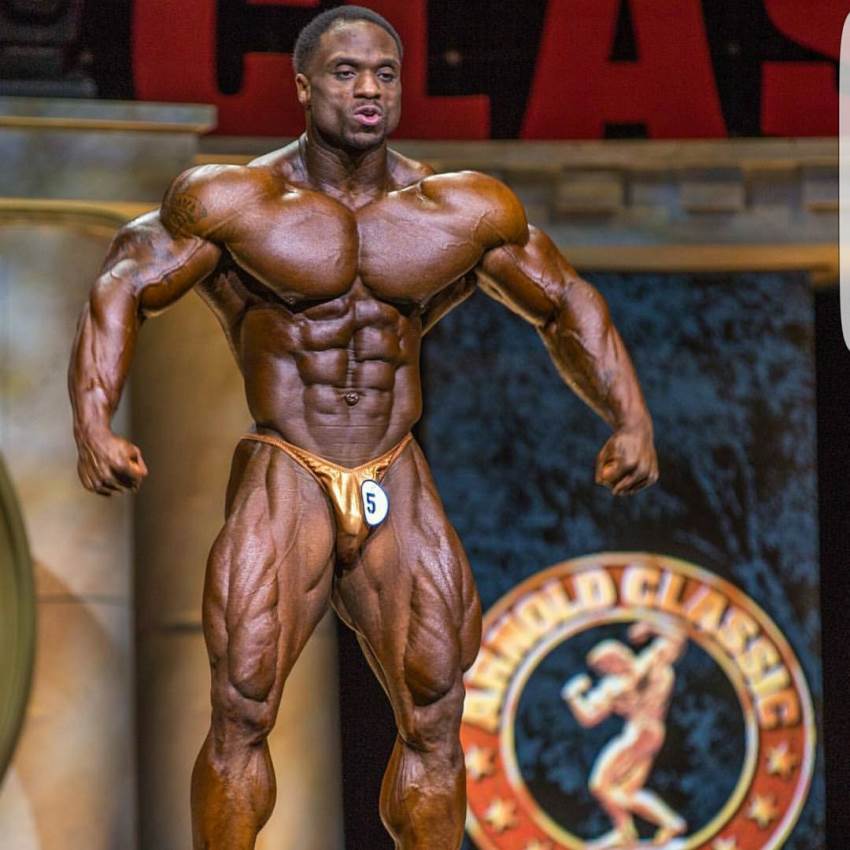 Michael Lockett confidently standing on the Arnold Classic stage, spreading his ripped arms and lats wide