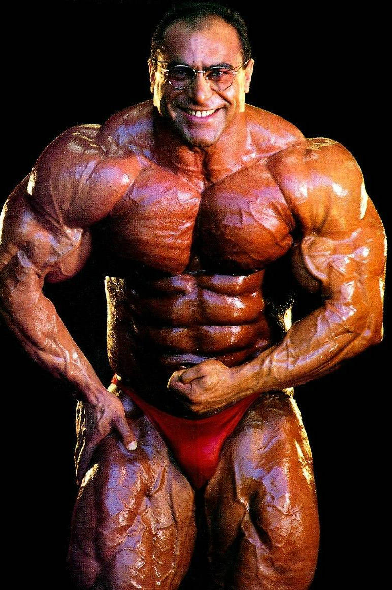 Nasser El Sonbaty posing before a competition, showing his ripped abs and massive arms