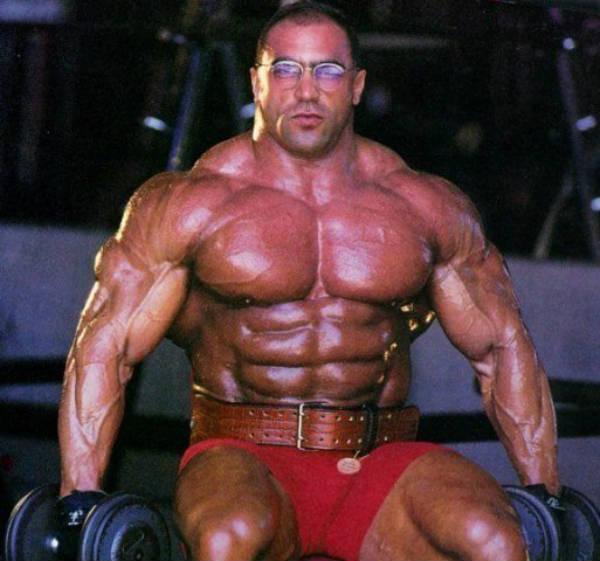 Nasser El Sonbaty sitting in the gym with a weight lifting belt, showing off his large abdominal muscles