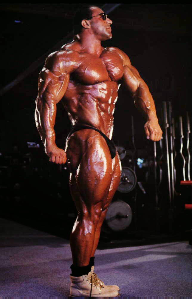 Nasser El Sonbaty showing his side profile, wearing military boots and displaying his ripped abs and well-built chest