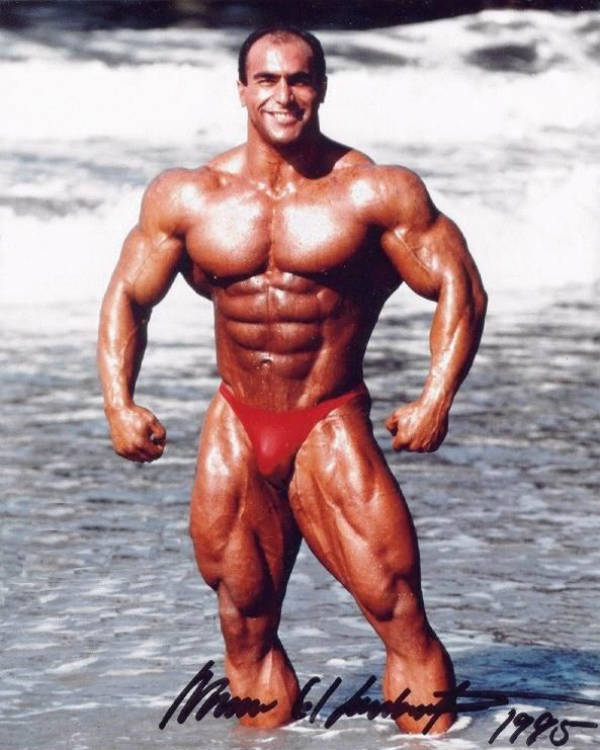 Nasser El Sonbaty standing in the sea and showing his full body, displaying his massive deltoids and large chest