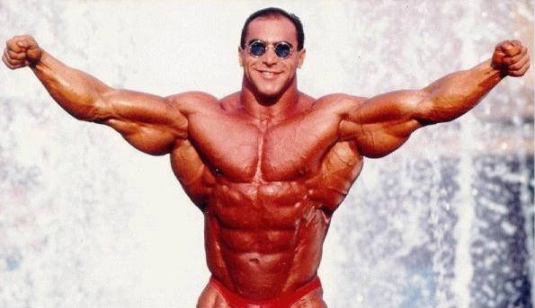 Nasser El Sonbaty with his arms raised to the side, showing his large triceps, chest and abs