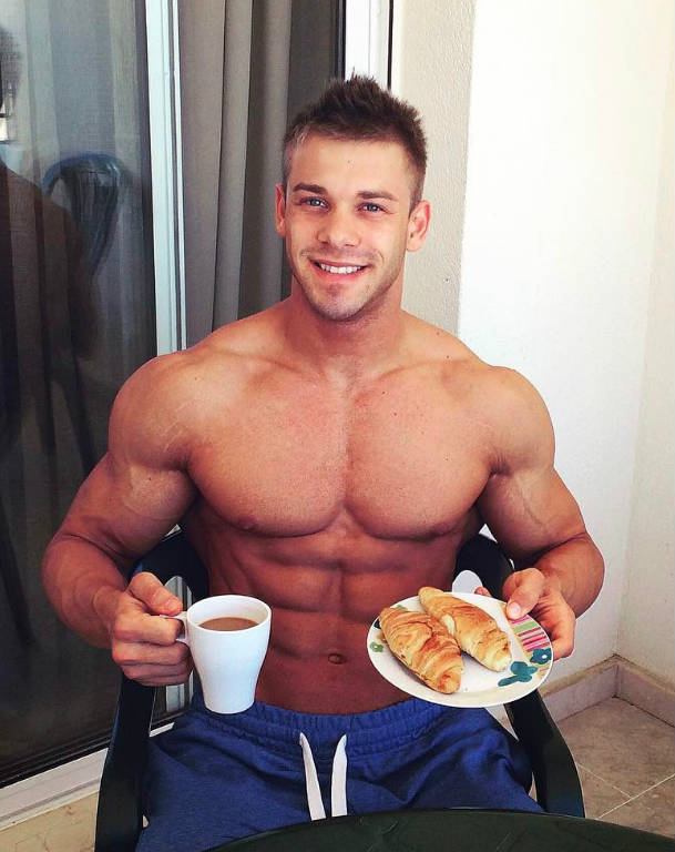 Ondrej Kmostak sitting down, eating a healthy meal and showing his large chest, abs and arms