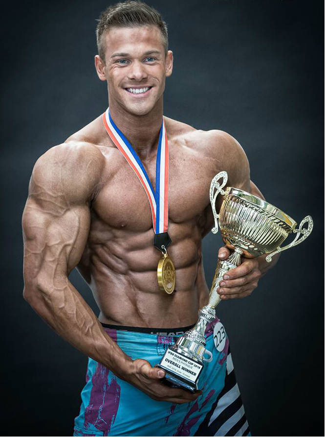 Ondrej Kmostak holding the winners trophy at a competition, displaying his ripped abs and large arms