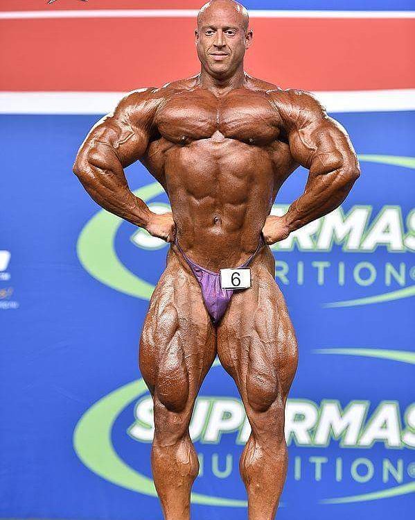 Petar Klancir on the stage, in a front lat spread pose, showing his extremely ripped physique to the audience