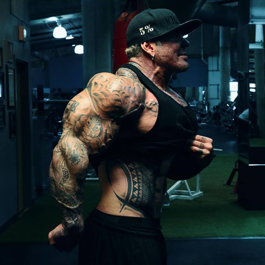 Rich Piana showing his monstrous arms from the side, as well as doing vacuum while lifting his black tank top