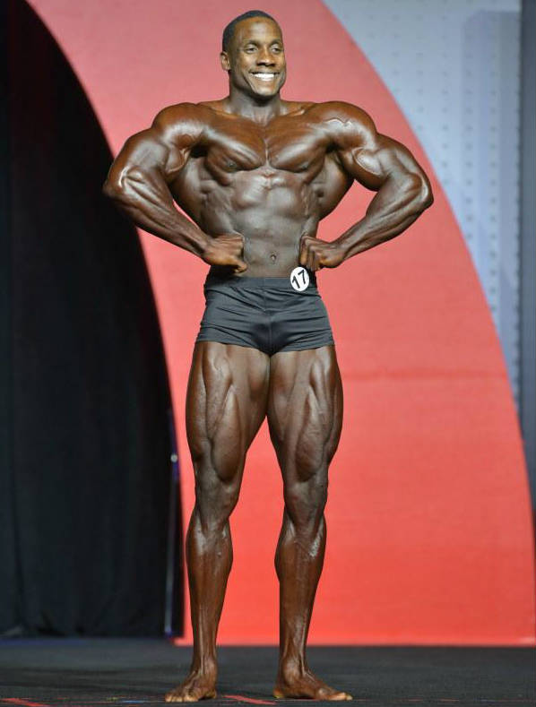 Robert Timms posing at a classic physique competition, showing his large chest, quads and arms