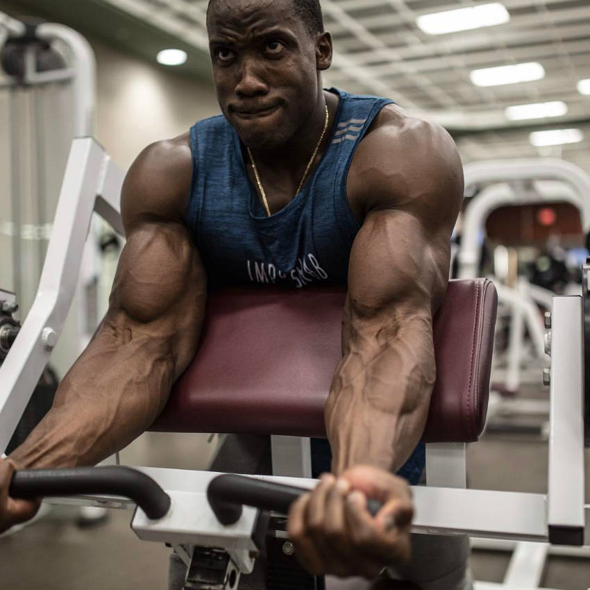 Robert Timms completing a bicep curl on the machine, showing his bulging biceps and vascular arms