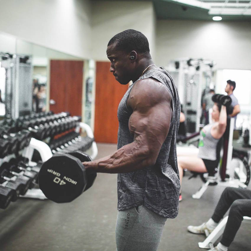 Robert Timms completing a bicep curl with a 40 kilo barbell, displaying his large arms 