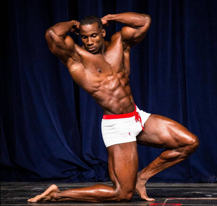 Robert Timms kneeling down at a competition, showing his large quads, obliques, abs and arms