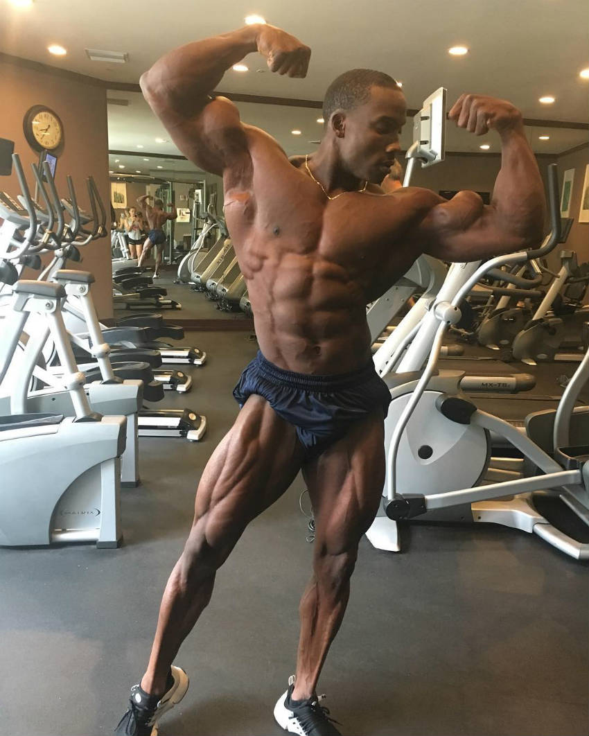 Robert Timms showing his full body in the gym, showing off his large quads, biceps and abs