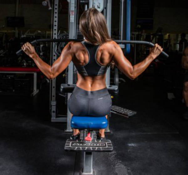 Taylor Chamberlain completing a lateral pull down, showing her pumped lats, toned delts and glutes