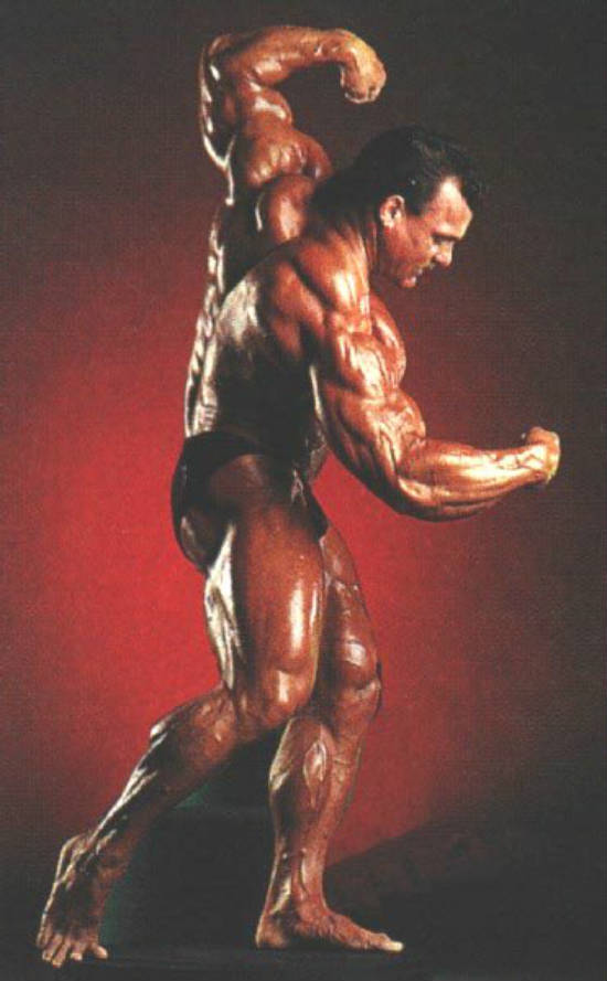Tim Belknap posing in a professional shot, showing his large biceps, arms and legs