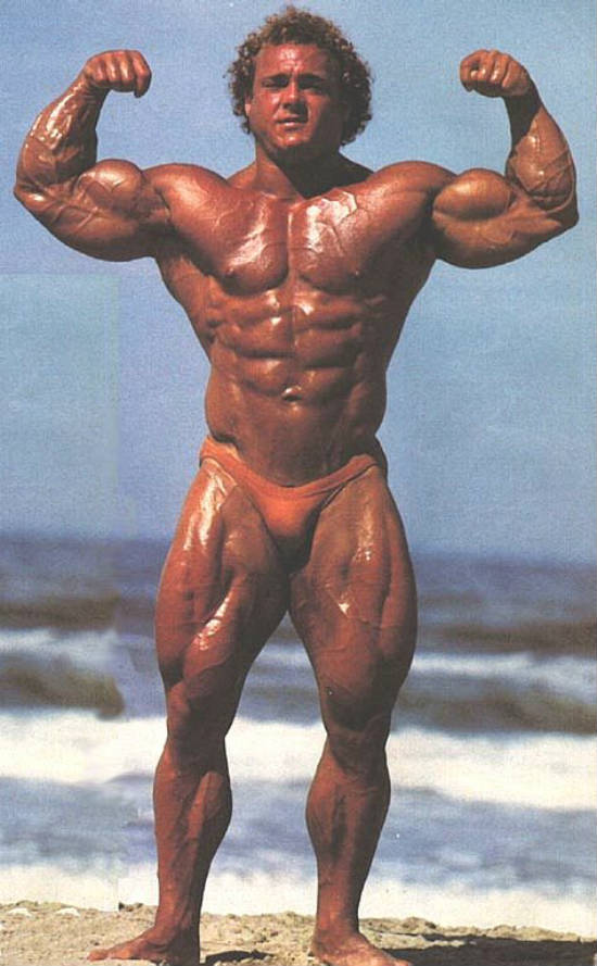 Tim Belknap standing on the beach showing his full ripped, toned and lean physique