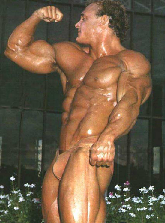 Tim Belknap tsnsing his bicep at a competition, showing his large biceps, abs, arms and chest