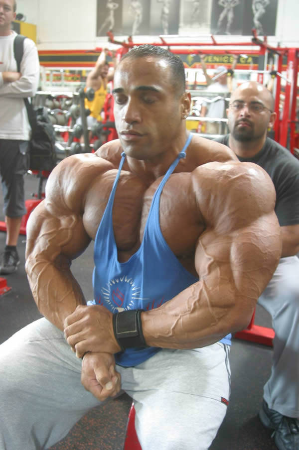 Dennis James sitting on a bench, showing his large arms, chest and quads