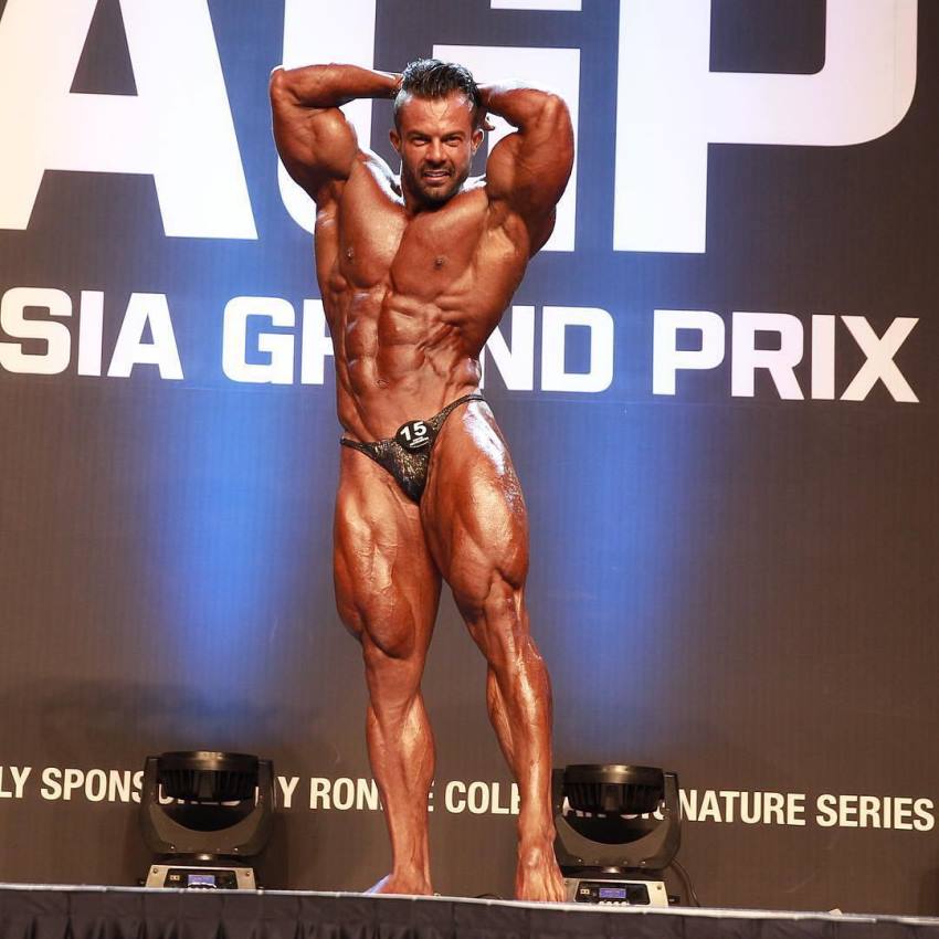 Babak Akbarniya posting on the Grand Prix bodybuilding stage, flexing his legs and abs, looking ripped and big